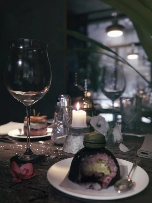 Wizualizacja pokazuje zbliżenie na drewniany blat stolika w restauracji, na stole jest ułożona zastawa z kieliszkami na wino, talerzami z ciastkami i świeczką